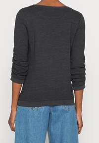 Heather black long-sleeve top with a textured pattern, slightly slouchy fit, and ribbed cuffs, paired with light wash, relaxed-fit jeans.