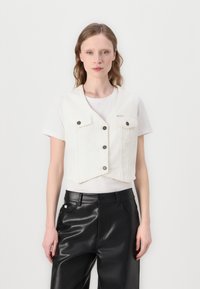 Hvit cropped denimvest med to brystlommer og sølvknapper, brukt over en hvit T-skjorte og kombinert med svarte skinnbukser.