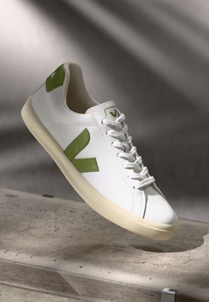 White sneaker with green suede accents and lace-up design. Smooth leather upper, textured rubber sole, and logo on tongue.