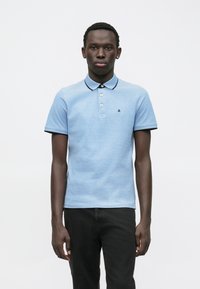 Lichtblauw polo shirt met korte mouwen, zwarte rand op de kraag en de mouwuiteinden, drie-knopen sluiting en klein logo op de borst.