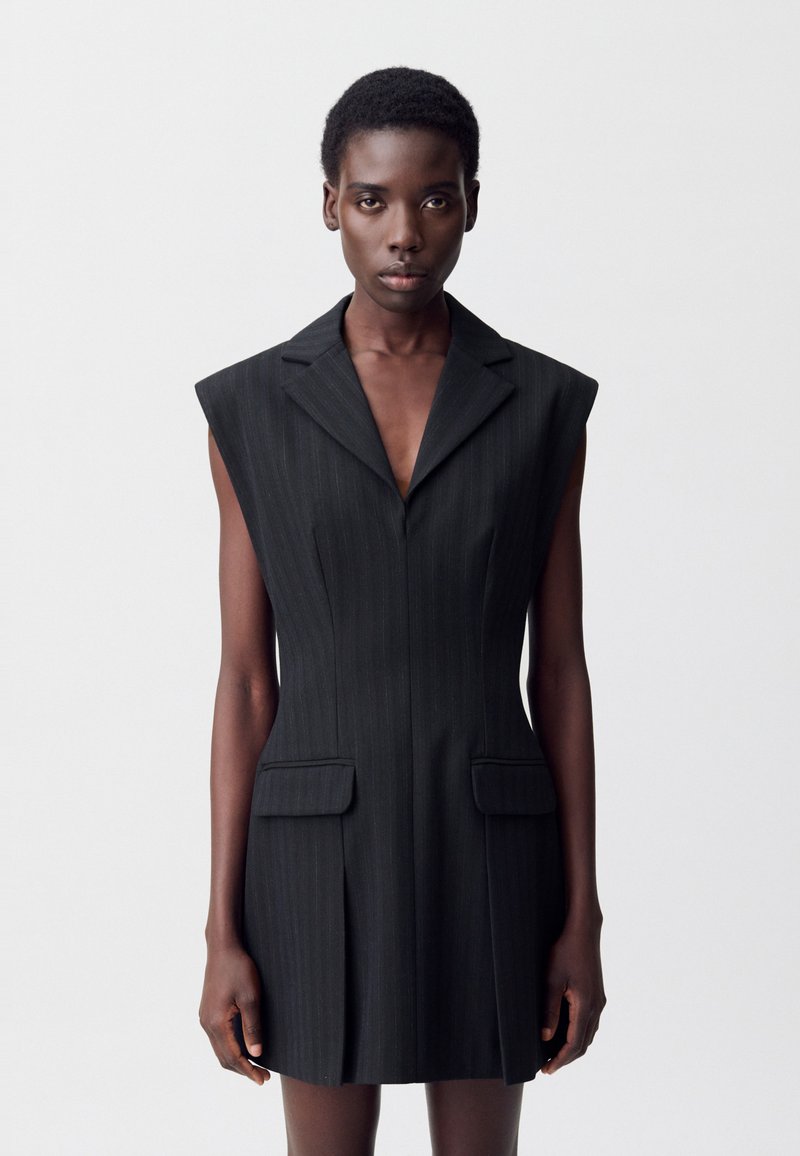 Abito senza maniche a righe nere con un colletto affilato, caratterizzato da due tasche frontali e una vestibilità su misura. Texture liscia con una silhouette moderna.