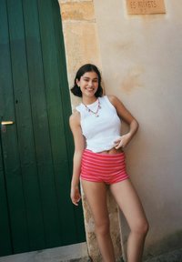 Et hvidt ærmeløst top og lyserøde shorts med striber, der fremhæver en glat stoftekstur og en tætsiddende pasform, med en farverig perlekæde.