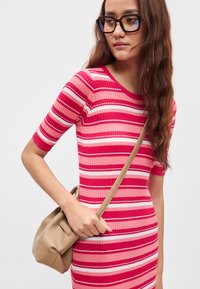 Ριμπ φόρεμα που αγκαλιάζει το σώμα με οριζόντιες ροζ και λευκές ρίγες. Το μοντέλο κρατά μια μικρή, ανοιχτό μπεζ τσάντα με λουράκι ώμου.