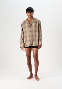 Brun rutig överdimensionerad skjorta i lätt tyg, med sned krage och knappar, kombinerad med svarta shorts.