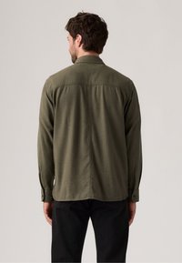 Olive green flannel shirt with long sleeves, a collar, and buttoned cuffs. Smooth texture with a slightly loose fit and back seam detail.
