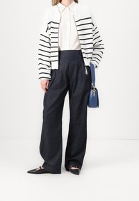 Świeżość biało-czarnego kardiganu w paski zestawionego z jasną koszulą rozpinaną, połączonego z ciemnoniebieskimi, szerokimi spodniami dżinsowymi oraz czarnymi, spiczastymi balerinami. Niebieska torba na ramię.