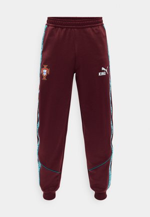 Pantaloni de trening bordo cu dungi laterale cu model teal, manșete elastice, emblema de fotbal a Portugaliei pe partea stângă și logo-ul alb Puma cu textul „KING” pe coapsa dreaptă.