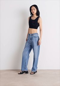 Svart cropped topp med elastisk kant, lyseblå høytlivsjeans og svarte sandaler med stropper, mot en enkel bakgrunn.