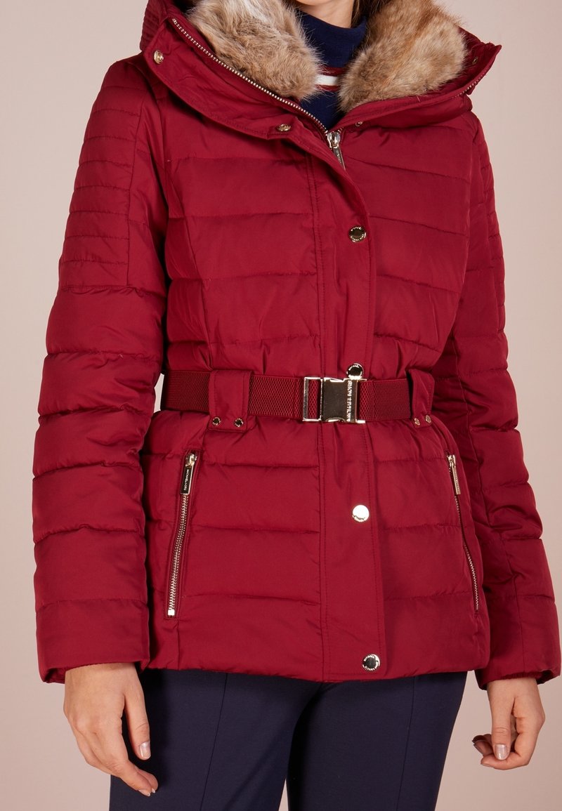 Punainen toppatakki, jossa tekoturkistettu huppu, vinottain tikattu pinta, vyötärösolki ja vetoketjulliset sivutaskut. Hopeanväriset metalliosat.
