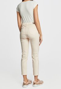 Jeans skinny beige claro con cintura alta, que cuentan con bolsillos traseros y costuras laterales. Combinados con zapatillas casuales rosas.