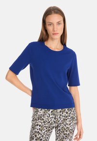 Short-sleeve blue top made from a smooth fabric with a crew neckline. Paired with patterned green and brown animal print trousers.