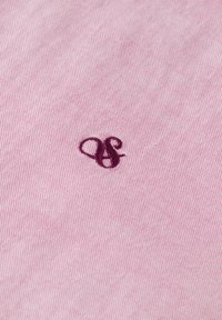 Tejido de algodón con hilo en color rosa claro con un fino patrón de cuadros. Presenta un logo bordado en color marrón con elegantes curvas.