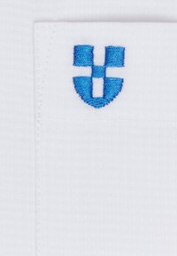 Biały materiał o teksturowanej powierzchni, z niebieskim haftowanym logo przypominającym stylizowaną literę 'Y' w kształcie tarczy na kieszeni.