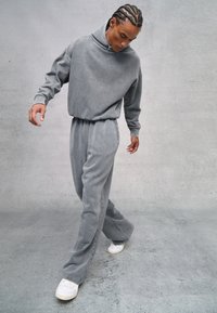 Grau Fleece-Trainingsanzug mit hohem Kragen und elastischem Bund. Lockere Hose und Oberteil; mit Logo-Stickerei. Kombiniert mit weißen Sneakern.
