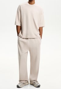 Beige oversized t-shirt with short sleeves paired with matching loose-fit trousers, both made from soft material, featuring clean lines.