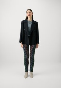 Crna dvoredna blazer jakna preko sive majice, uparena s legginama s višebojnim uzorkom i bež čizmama na pete do gležnja.