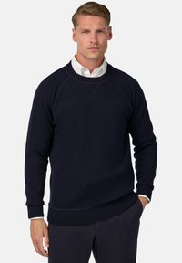 Tamsiai mėlynas megztinis su apvalia iškirpte, pagamintas iš minkštos medžiagos, su raglano rankovėmis, gumbuotais rankogaliais ir paprastu dizainu su lygiu paviršiumi.