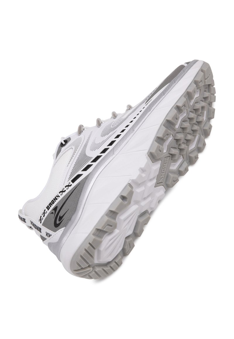 Zapatilla deportiva blanca con una suela gris texturizada, que presenta un acento de diseño en plata y negro, con sujetadores de cordones visibles y una forma aerodinámica.