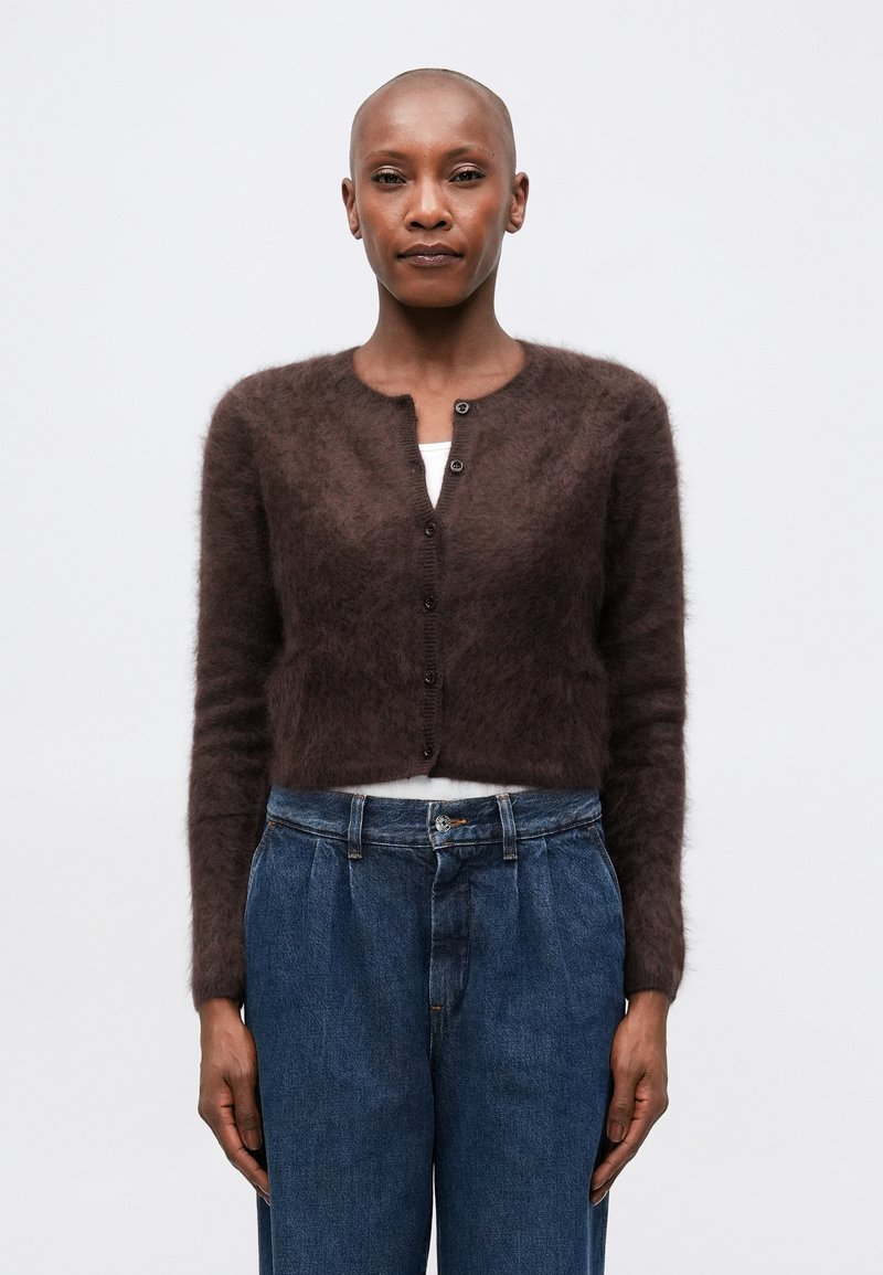 Cardigan marrón esponjoso con escote redondo, mangas largas y cierre de botones en la parte delantera, combinado con pantalones de mezclilla azul de tiro alto.