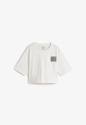 Camiseta recortada de manga corta en algodón crema con un patrón gráfico en azul marino en la zona del bolsillo del pecho. Cuello redondo y diseño de corte holgado.