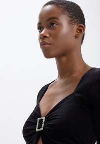 Top in velluto nero con un design a fronte attorcigliato, caratterizzato da una fibbia rettangolare decorata con cristalli all'collo, texture liscia e forma aderente.