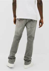 Jeans din denim gri cu croială dreaptă, având cusături decorative pe buzunarele din spate, purtate cu o cămașă albă și adidași albi.