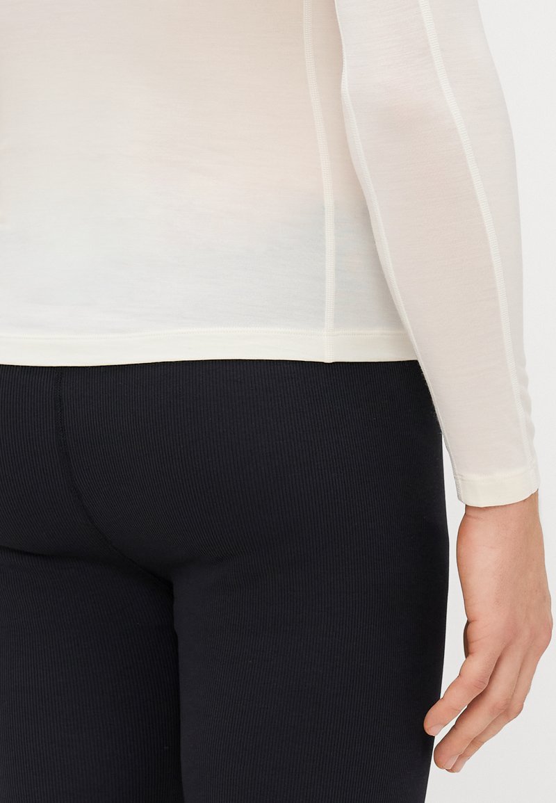 Top leggero a maniche lunghe di un bianco crema, con un design aderente e una sottile texture a coste; abbinato a leggings neri a coste.