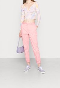 Cropped tie-dye long-sleeve top in pastel colors, paired with pink tapered pants. Accessorized with a light purple handbag and sneakers.