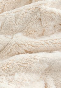 Material moale din fleece de culoare crem, cu un strat gros și texturat, prezentând pliuri delicate și un aspect pufos și confortabil.