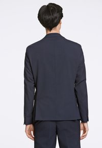 Giacca da completo blu navy con taglio su misura, caratterizzata da una texture liscia, rever a incavo e quattro bottoni su ogni polsino.