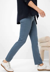 Pantaloni slim-fit azzurro chiaro realizzati in misto cotone, caratterizzati da linee pulite e un tessuto leggermente testurizzato, abbinati a sneaker bianche con accenti chiari.