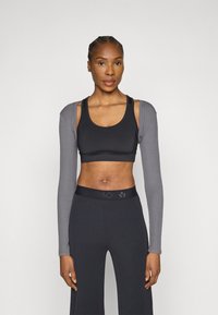 Sort atletisk BH med grå ermer i glatt stoff, tettsittende design og bred linning med subtil logo.