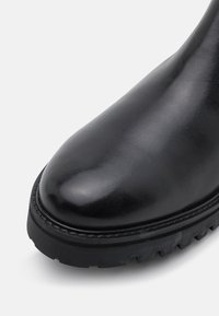 Czarne skórzane botki za kostkę o gładkim wykończeniu, okrągłym nosku i wytrzymałej czarnej gumowej podeszwie z głębokim bieżnikiem zapewniającym przyczepność.