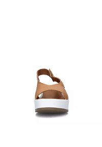 Sandal in pelle marrone con design aperto, suola piattaforma bianca e cinturino regolabile sul retro. Accenti intagliati notevoli sui lati.
