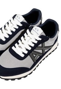 Zapatillas deportivas con una parte superior de malla gris, acentos de gamuza azul marino, cordones blancos y una suela de goma negra. Presenta un logo en la lengüeta.