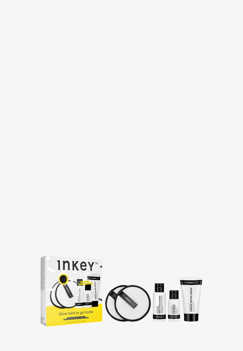 Set de soins de la peau dans une boîte avec des accents jaunes vifs. Comprend deux coussinets ronds blancs et trois bouteilles de produit noir et blanc.