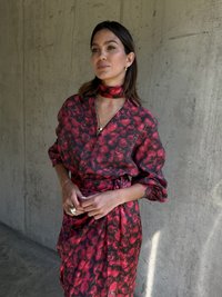 Červená blůza a sukně se květinovým vzorem vyrobené z lehkého materiálu. Blůza má zapínání na knoflíky a široké rukávy, doplněná o ladící šátek.