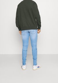 Sudadera verde oscuro, vaqueros pitillo azul claro, zapatillas blancas con detalles en rojo y azul. Enfoque en texturas y diseño sencillo.