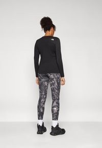 Sort langærmet top, tætsiddende. Grå mønstrede leggings med sort og hvide elementer. Sorte træningssko, hvide sokker.