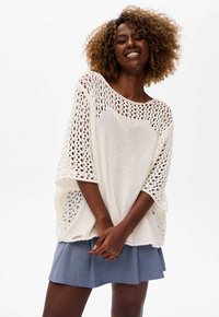 Weißer, locker gestrickter Pullover mit weitem Schnitt, kurzen Ärmeln und rundem Halsausschnitt, kombiniert mit einem blauen Faltenrock.