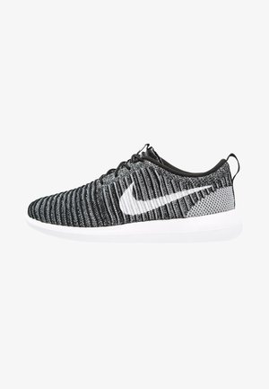 Svart och grå stickad Nike löparsko med vit swoosh-logotyp och vit sula, sedd från sidan.