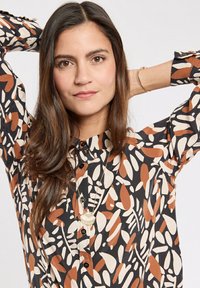 Long-sleeve blouse featuring a black background with abstract leaf patterns in shades of orange, cream, and brown; finished with a button-up front.