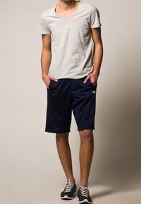 Gray short-sleeve V-neck t-shirt paired with dark navy athletic shorts, featuring side pockets and logo detail, worn with black athletic shoes.