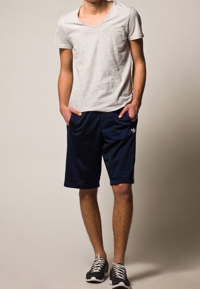 Gray short-sleeve V-neck t-shirt paired with dark navy athletic shorts, featuring side pockets and logo detail, worn with black athletic shoes.