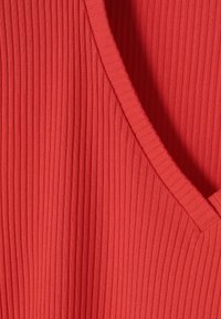 Hladký pletený materiál v živé červené barvě. Jemná textura se zaobleným výstřihem a mírným elastickým účinkem, s elegantním, přiléhavým střihem.