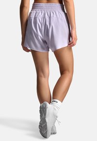 Lyse lilla atletikshorts med elastisk talje, glat tekstur og løs pasform, kombineret med hvide sneakers og crew-strømper.