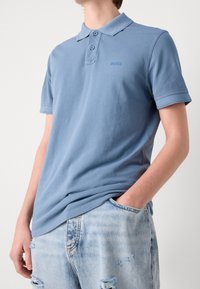 Jasnoniebieska koszulka polo z kołnierzykiem, dwoma guzikami i wyhaftowanym logo "BOSS". Połączona ze spodniami dżinsowymi w jasnym kolorze z przetarciami.