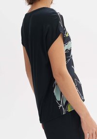Svart topp med korta ärmar och färgglatt abstrakt mönster på sidan och ryggen, tillverkad av lätt och mjukt tyg. Avslappnad passform och djup rund halsringning.