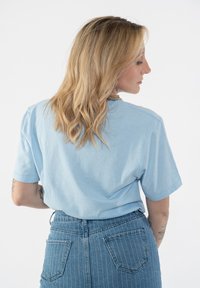 Light blue cotton t-shirt with short sleeves and a relaxed fit, paired with high-waisted striped denim jeans featuring back pockets.