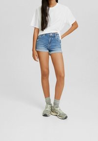 Ljusblå denimshorts med upplagda fållar, kombinerade med en vit t-shirt med kort ärm och grå sportskor med matchande strumpor.